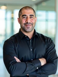 Professional headshot of a man with close-cropped hair and trimmed beard, wearing a black button-down and smiling in a bright office; Medical Director at YOU. A MedSpa in Arroyo Grande, CA.